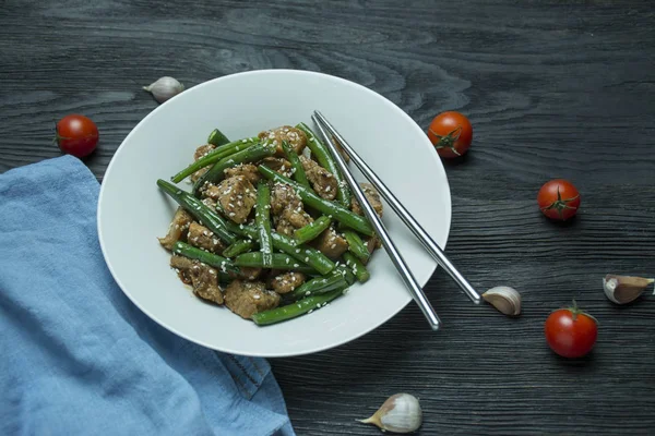 Салат из зеленой фасоли и мяса, посыпанный семенами кунжута. Подача горячего салата с зелеными бобами. Азиатская еда. Темный деревянный фон. Пространство для текста . — стоковое фото