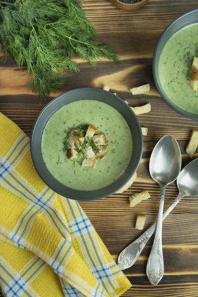 Creamy spinach soup with crackers, herbs and chia seeds. Green soup served in a bowl on a wooden table. Flat lay.