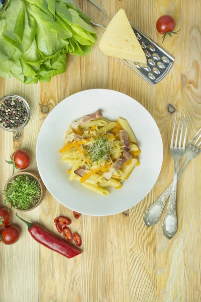 Peynirli İtalyan makarnası, balkabağı ve kızarmış domuz pastırması, beyaz tabakta servis ediliyor. Hafif ahşap arkaplan.