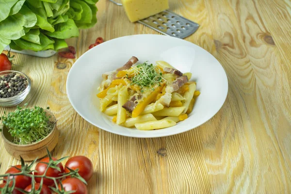 Peynirli İtalyan makarnası, balkabağı ve kızarmış domuz pastırması, beyaz tabakta servis ediliyor. Hafif ahşap arkaplan.