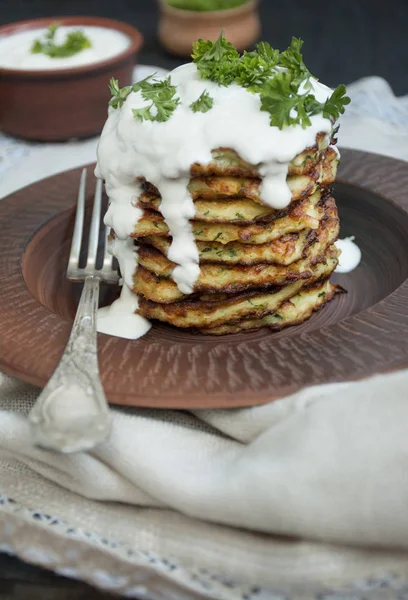 Zucchini fritters. Vegetarian zucchini pancakes with fresh herbs and sour cream. A stack of pancakes. Dining table. Balance healthy food. Light background.