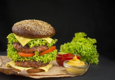Ready-made hamburger with beef cutlets, cheese, cucumber, fresh tomatoes and salad on a dark background. Fast food. Cooking. Copy space. Place for text.