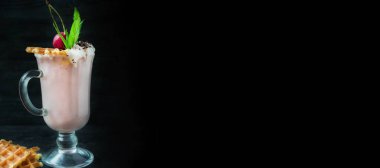 Dondurmalı vişneli milkshake, krema, marşmelov, kurabiye, waffle, koyu arkaplanda cam bir fincanda servis edilir. Yaz içeceği. Pankart. Metin için boşluk.
