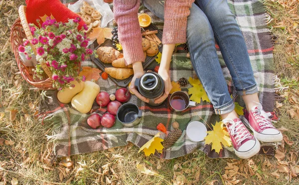 Autumn picnic in the park, warm autumn day. The girl holds a thermos in her hands with tea. Basket with flowers, yellow autumn leaves. Autumn concept.