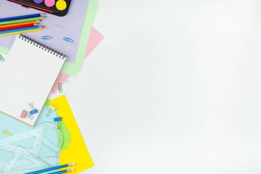 Beyaz bir arka planda okul malzemeleri. Çok renkli tahta kalemler, defter, ataç, cetvel, kağıt çıkartmalar. Ofis aletleri. Eğitim kavramı kopyalama alanı