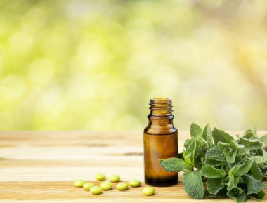 Cam bir şişede naneli yağ ve ahşap bir masada taze nane yaprakları. Boşluğu kopyala.