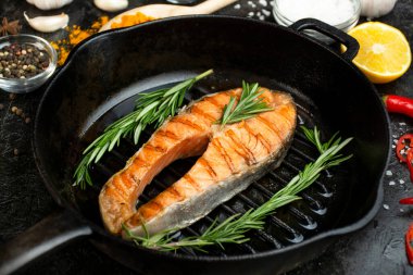 Izgara tavada somon bifteği ve karanlık bir masada baharatlar.