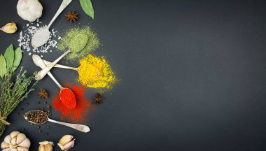 Karanlık bir masada kaşıklardaki çeşitli baharatlar ve otlar. Yemek için baharat. Yemek arkaplanı. Pankart. Boşluğu kopyala.