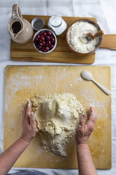 Hands, old womens, knead the dough of butter and flour and water on a wooden board on the table. Cooking in home. Joint family pastime on self-isolation. Chopped dough recipe - the third stage.