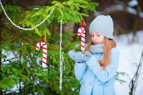 青いコートで凍るような冬の日の屋外に飾られたクリスマス ツリーの近くに立ってミトンにかわいい笑顔の少女の肖像画. — ストック写真