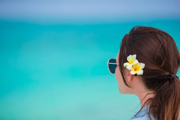 Крупним планом красива жінка під час тропічних пляжних канікул. Насолоджуйтесь літнім відпочинком наодинці на пляжі з квітами франгіпані у волоссі — стокове фото