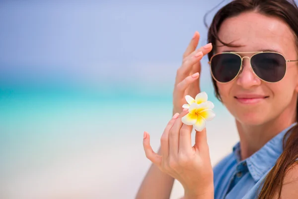 Joven hermosa mujer durante las vacaciones en la playa tropical. Disfrute de vacaciones suumer solo en la playa con flores de frangipani en su cabello — Foto de Stock