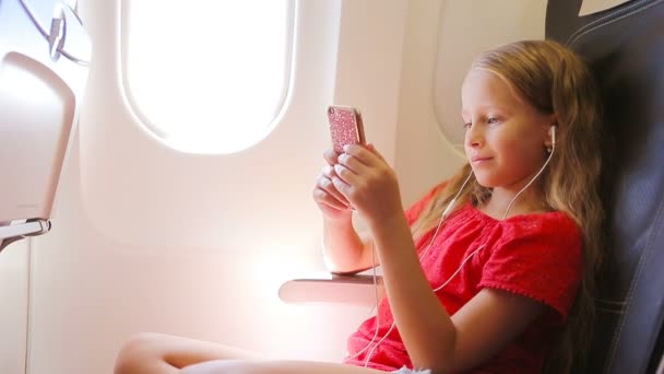 Menina adorável viajando por um avião sentado perto da janela. Kid ouvindo música sentada perto da janela da aeronave — Vídeo de Stock