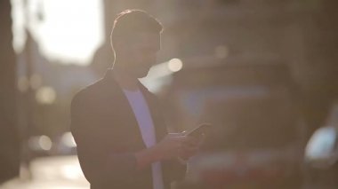 Genç adam açık havada, hafif ışıkta cep telefonu kullanıyor.