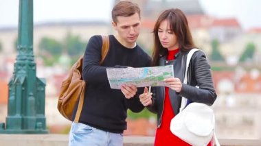 Avrupa 'da tatil yapan genç turist çift mutlu bir şekilde gülümsüyor. Şehir haritası olan beyaz bir aile cazibe arıyor.