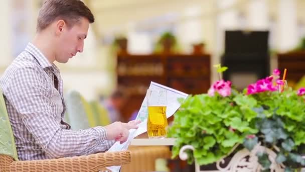 Kaukasische jonge Europeaan met stadsplattegrond in een café buiten. Portret van aantrekkelijke jonge toerist tijdens lunchtijd — Stockvideo