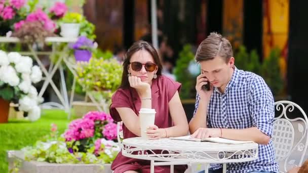 Pareja joven en la cafetería al aire libre. Chica joven está enojado con su novio porque él está ocupado con las tareas — Vídeos de Stock