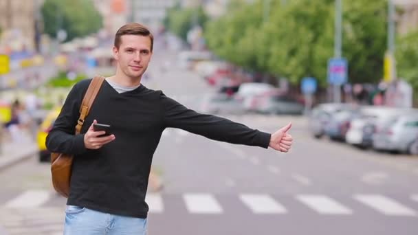 Jonge gelukkige man neemt een taxi in de Europese straten. Portret van een blanke toerist met een glimlachende rugzak en een taxi — Stockvideo