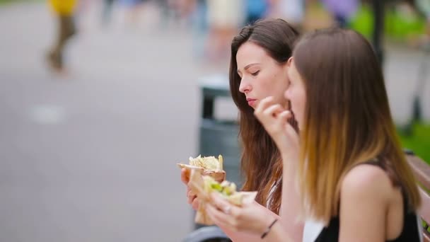 Белые женщины едят сэндвич с гамбургером на улице. Активные девушки голодные и едят уличную еду после долгой прогулки — стоковое видео
