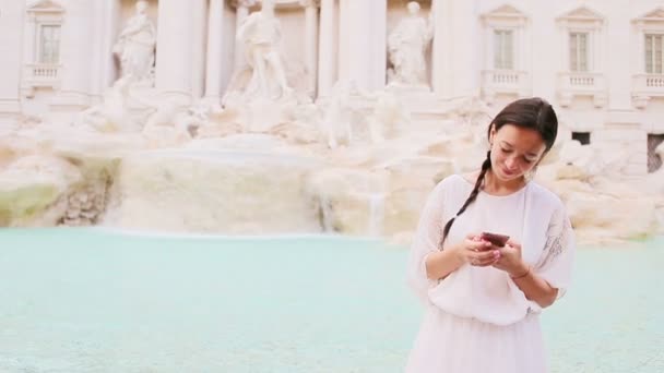 Mujer joven con teléfono inteligente en el cálido día al aire libre en la ciudad europea cerca de la famosa Fontana di Trevi — Vídeos de Stock