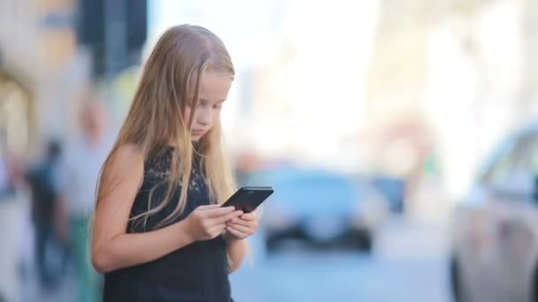 Adorable niña con teléfono inteligente en el cálido día al aire libre en la ciudad europea — Vídeo de stock