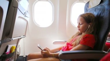 Pencerenin yanında oturan uçakla seyahat eden sevimli küçük kız. Müzik dinleyen ve mesaj gönderen çocuk uçak penceresinin yanında oturuyor.