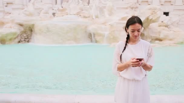 Молодая женщина со смартфоном рядом со знаменитым фонтаном Треви — стоковое видео