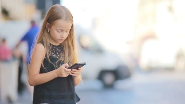 Schattig klein meisje met smartphone op warme dag buiten in europese stad — Stockvideo