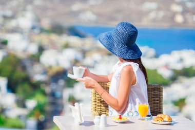 Mikonos kentine muhteşem manzaralı açık kafede kahvaltı güzel zarif bayan. Resort Restoran deniz manzaralı lüks otel terasında sıcak kahve içme kadın.