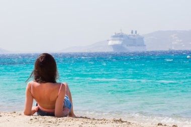 Sahilde arka planda genç bir kız. Kadınlar, Mykonos, Yunanistan ve Avrupa 'daki en güzel plajlardan birinde çiçeklerinin keyfini çıkarıyorlar..