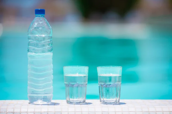 Szklanki wody i butelki na skraju basenu bez krawędzi — Zdjęcie stockowe
