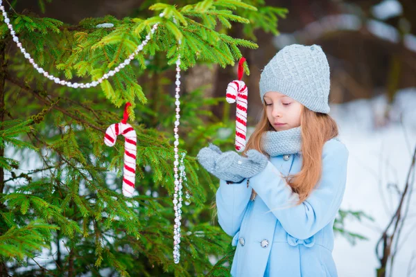 Portrait d'une petite fille mignonne et souriante en manteau bleu et mitaines debout près du sapin de Noël décoré lors d'une journée d'hiver givré en plein air . — Photo