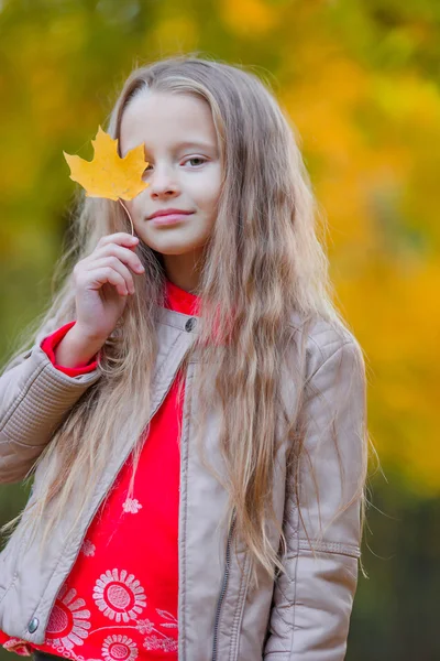 Adorable little girl outdoors at beautiful warm day in autumn park with yellow leaf in fall — Stock Photo, Image