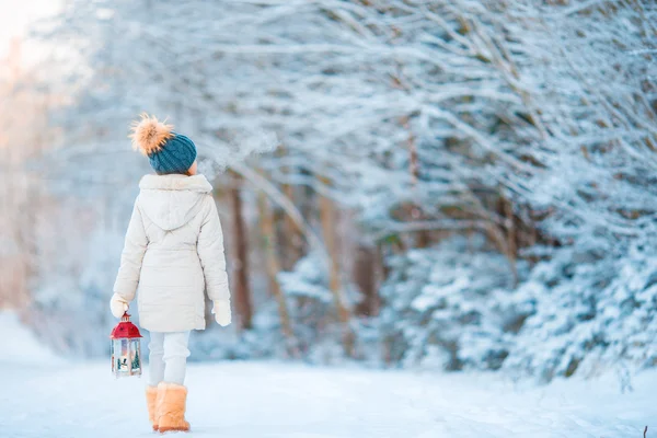 Adorable niña usando abrigo caliente al aire libre en el día de Navidad sosteniendo la linterna caminando —  Fotos de Stock