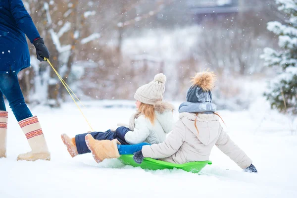 Маленькие девочки наслаждаются катанием на санках в зимний день. Отец катался на санках со своими очаровательными дочерьми. Семейный отдых в канун Рождества на природе — стоковое фото