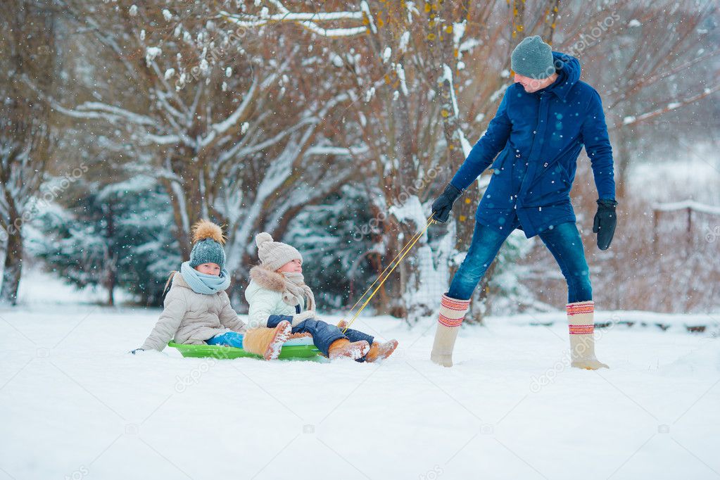 Little girls enjoying sledding in winter day. Father sledding his little adorable daughters. Family vacation on Christmas eve outdoors