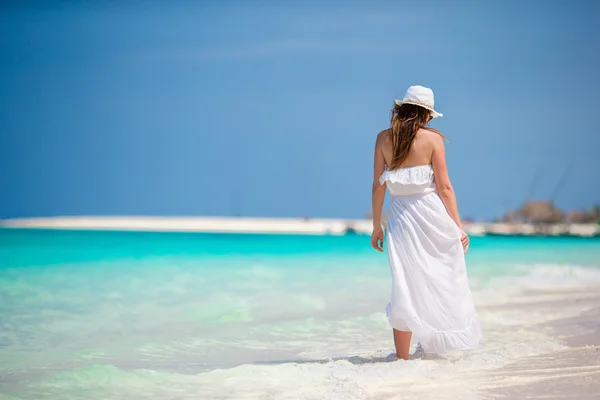 Joven hermosa mujer durante las vacaciones en la playa tropical. Disfruta de vacaciones de verano sola en la playa con flores de frangipani en el pelo —  Fotos de Stock