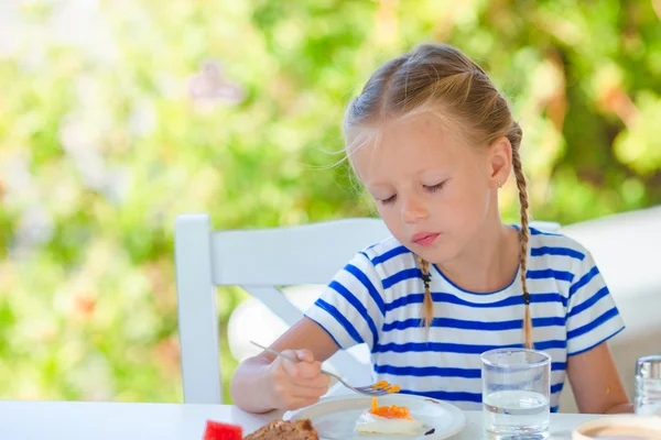 Adorable little girl having breakfast at outdoor cafe early in the morning — Stock Photo, Image