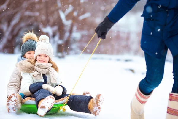Маленькие девочки наслаждаются катанием на санках. Отец катался на санках со своими очаровательными дочерьми. Семейный отдых в канун Рождества на природе — стоковое фото