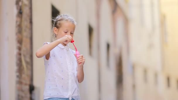 Egy kislány szappanbuborékokat fúj az európai város keskeny utcájában. Portré kaukázusi gyerek élvezze a nyári vakáció Rómában — Stock videók