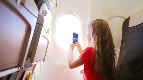 Entzückendes kleines Mädchen, das im Flugzeug am Fenster sitzt. Kind fotografiert Wolken und Himmel am Flugzeugfenster — Stockvideo