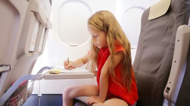 Uçakla seyahat eden sevimli küçük kız uçak penceresinde oturuyor. Renkli kalemlerle resim çizen çocuk. — Stok video