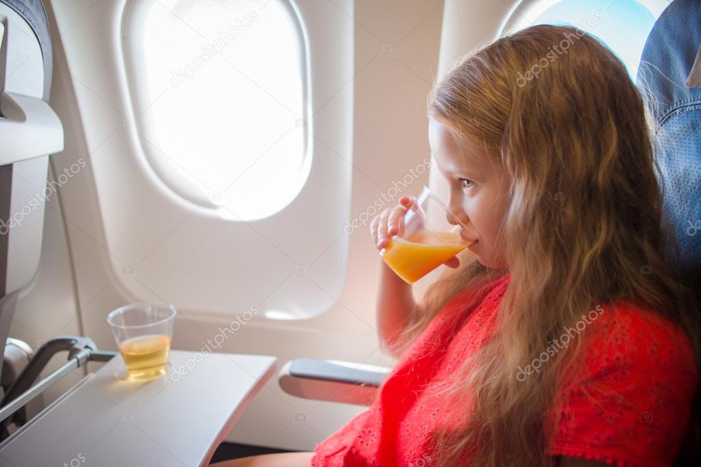 Adorable little girl traveling by an airplane. Kid drinking orange juice sitting near aircraft window