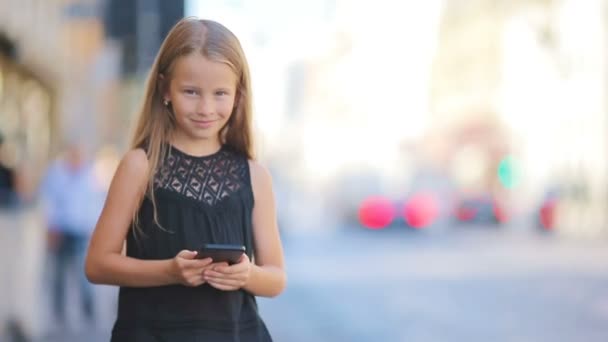 Adorable petite fille avec téléphone intelligent à la journée chaude en plein air dans la ville européenne — Video