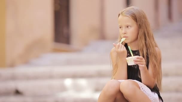 Очаровательная маленькая девочка ест мороженое на открытом воздухе летом. Милый ребенок наслаждается настоящим итальянским мороженым в Риме — стоковое видео
