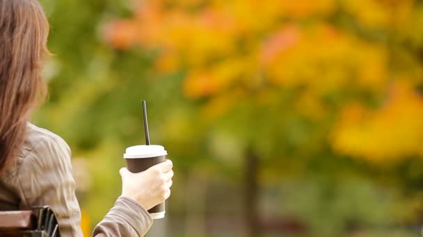 El concepto de otoño - la mujer hermosa que bebe café en el parque otoñal bajo el follaje otoñal — Vídeo de stock