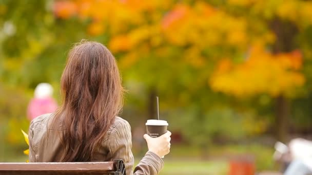 Mooie vrouw drinken koffie in de herfst park onder de herfst gebladerte — Stockvideo