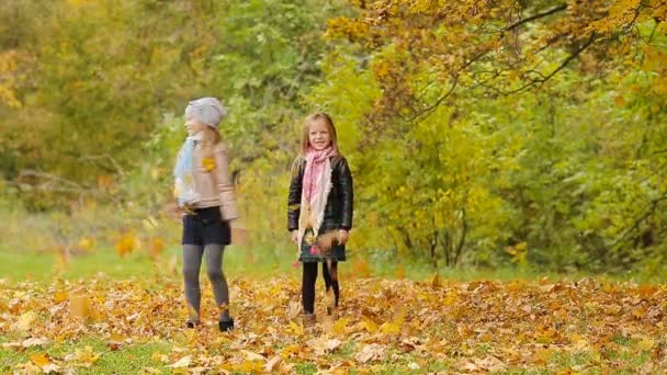 Маленькие очаровательные девочки веселятся с листьями в теплый день в осеннем парке на открытом воздухе — стоковое видео