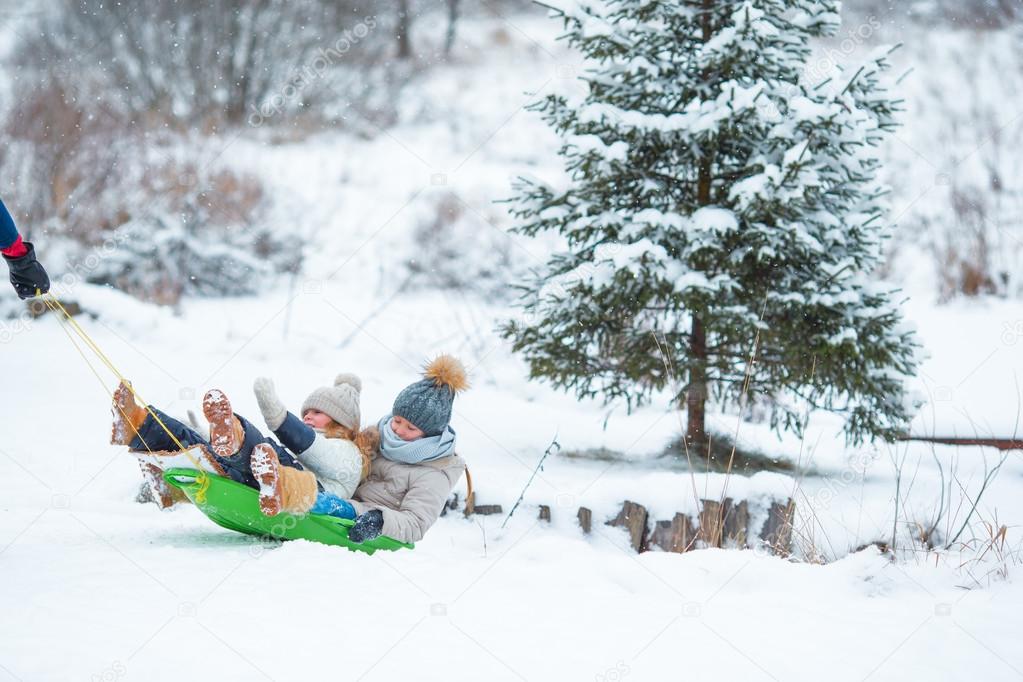 Little girls enjoying sledding in winter day. Father sledding his little adorable daughters. Family vacation on Christmas eve outdoors
