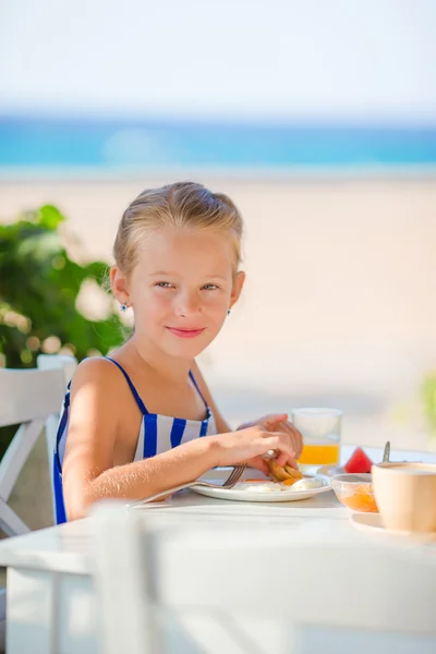 Красивая маленькая девочка завтракает в кафе с видом на море — стоковое фото
